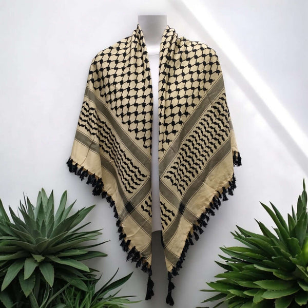 Off-white and black kufiya scarf with timeless geometric pattern and tassels displayed on mannequin amidst green plants